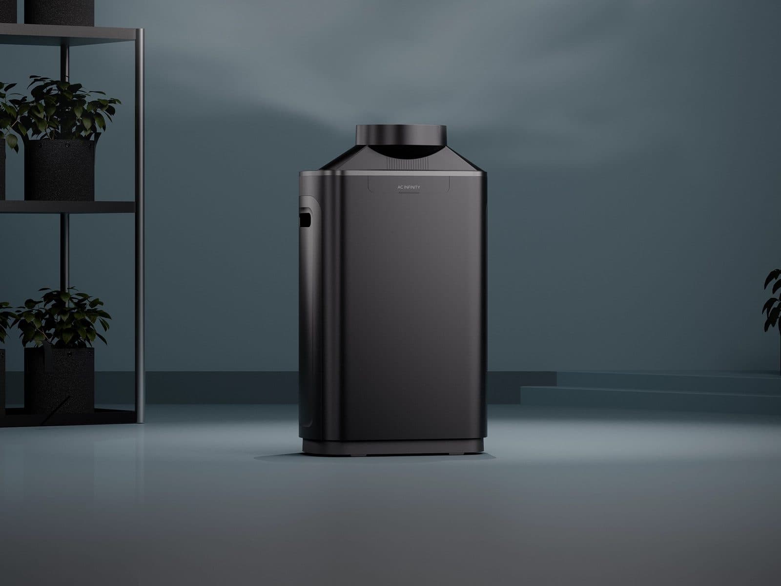 A black AC Infinity unit on a pale floor beside a shelf of potted plants, against a slate blue wall.