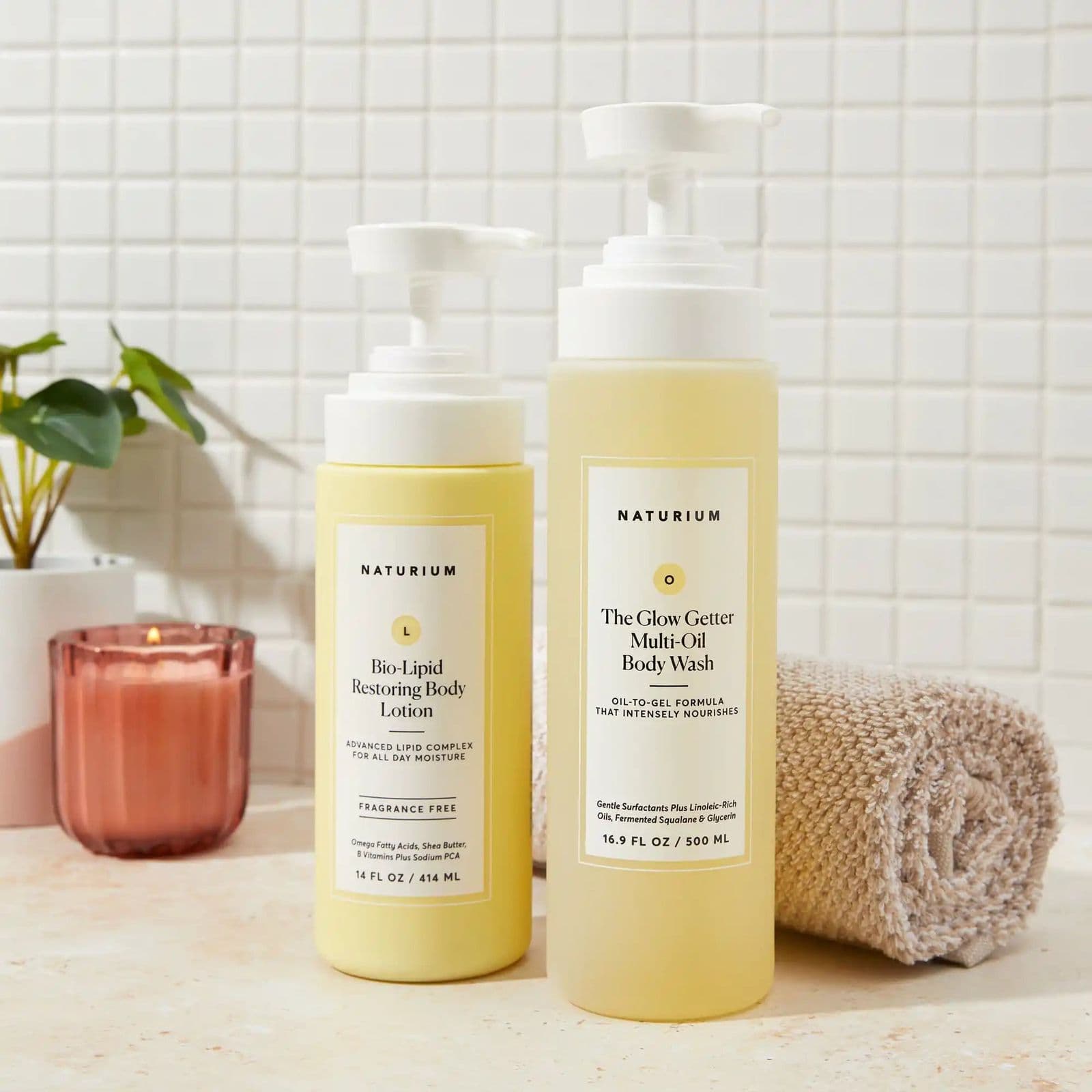Two pale yellow pump bottles on a stone bathroom counter beside a candle and a folded towel