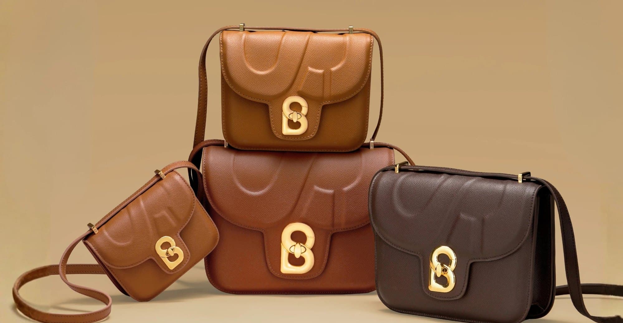 Four Buttonscarves leather shoulder bags in tan, cognac and dark brown, each with a gold B clasp, on a tan backdrop.