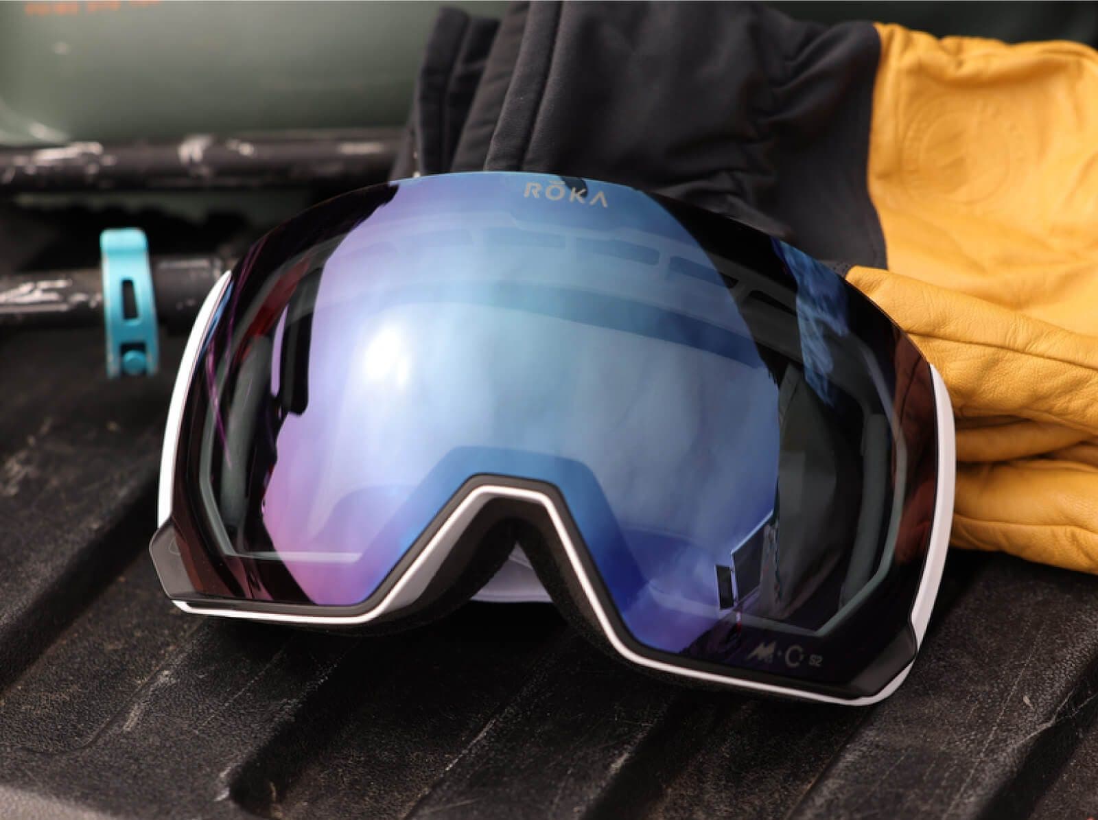 ROKA ski goggles with a blue mirrored lens resting on dark wood beside a yellow glove.