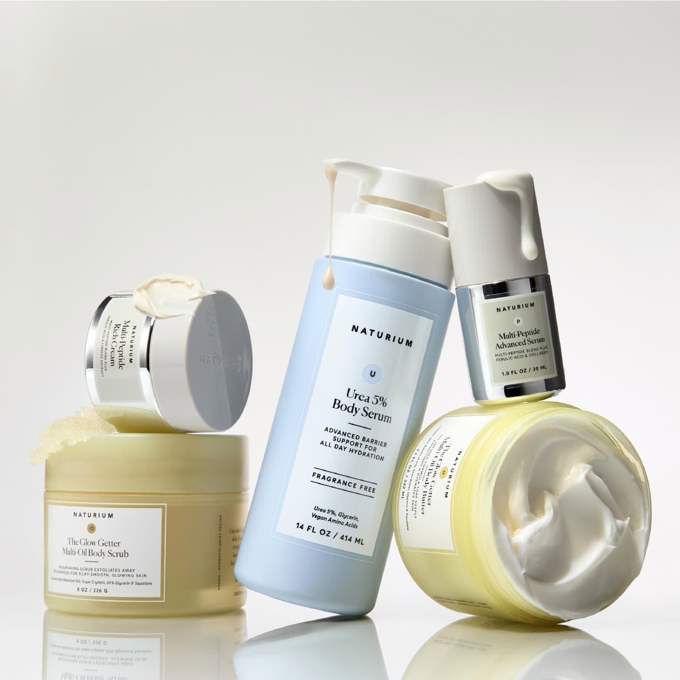Pump bottles and jars of skincare in pale yellow, blue and white, lined up on a white surface.