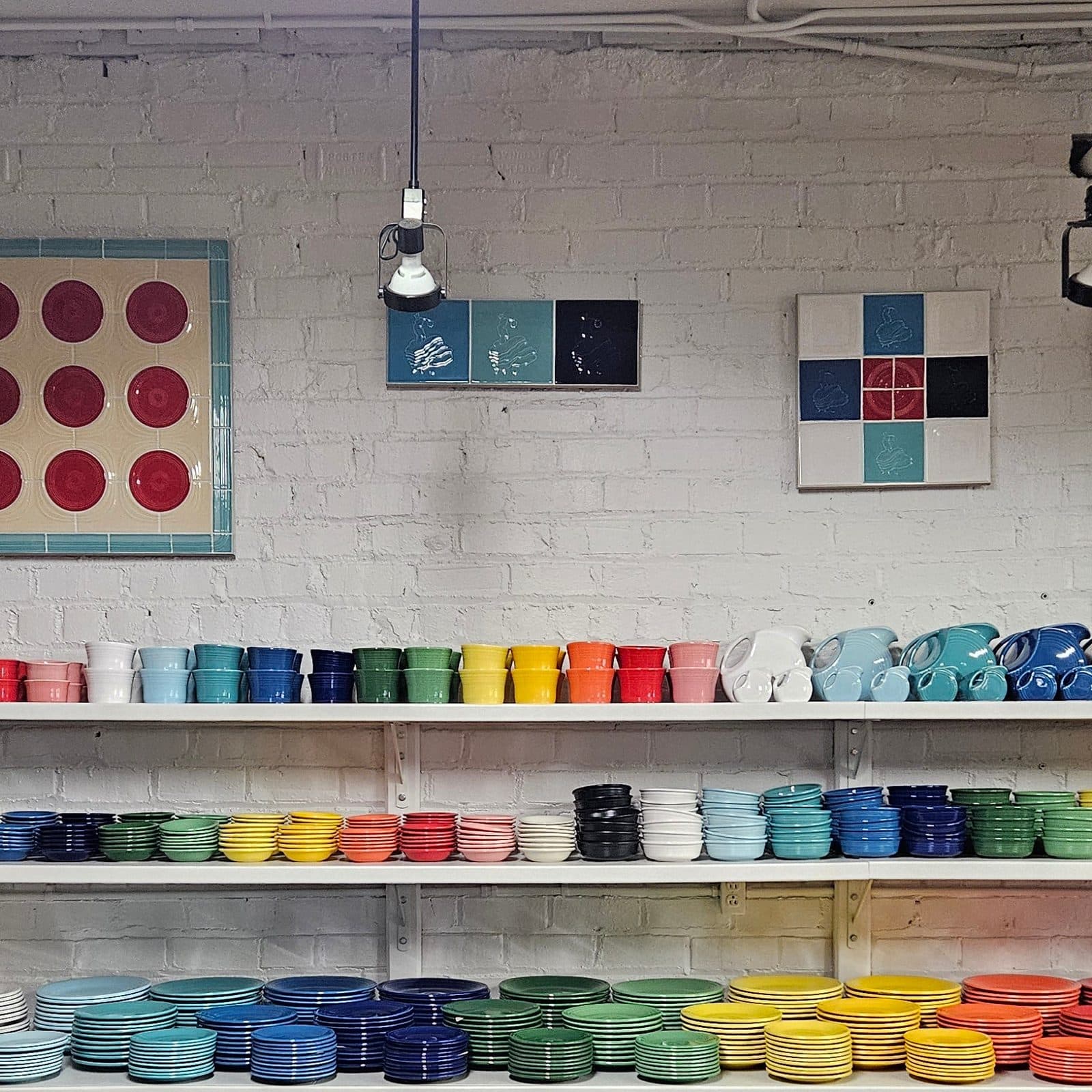 Inside a tableware shop: white shelves of mugs, bowls and plates sorted by colour under framed tile panels