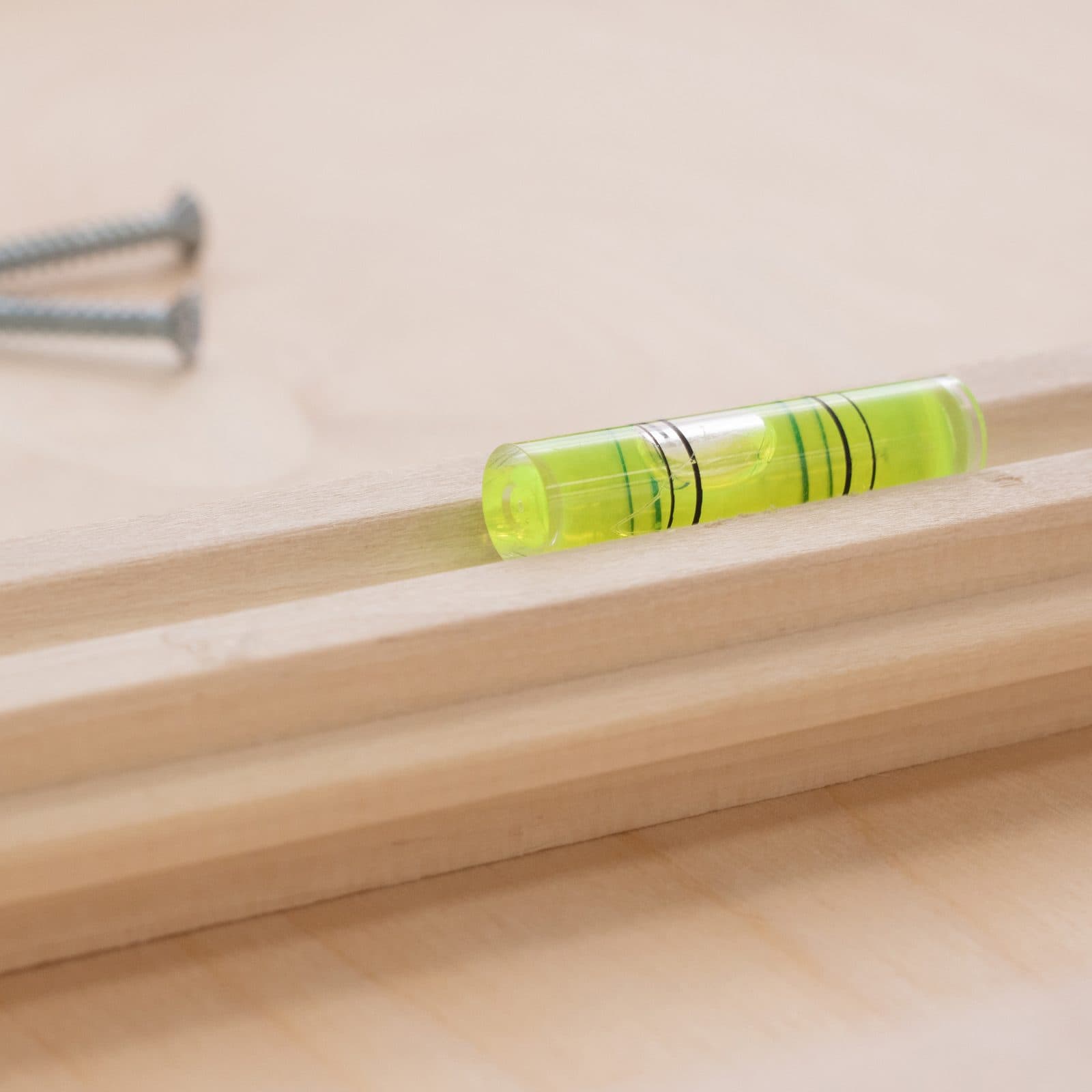 A yellow green bubble level set into a light maple wall cleat, two screws blurred behind it