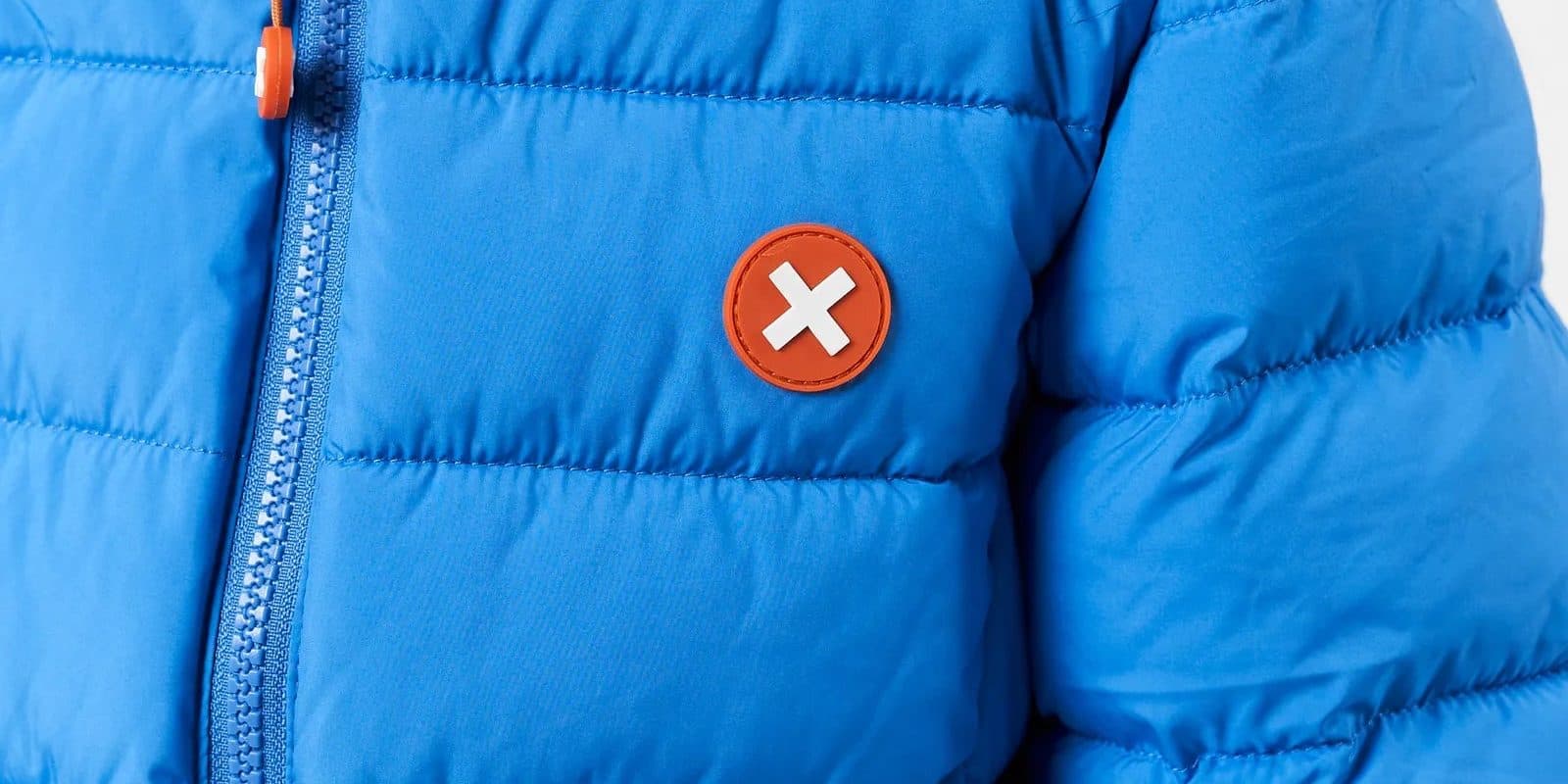 A bright blue puffer jacket with a round orange X patch on the chest beside the zip