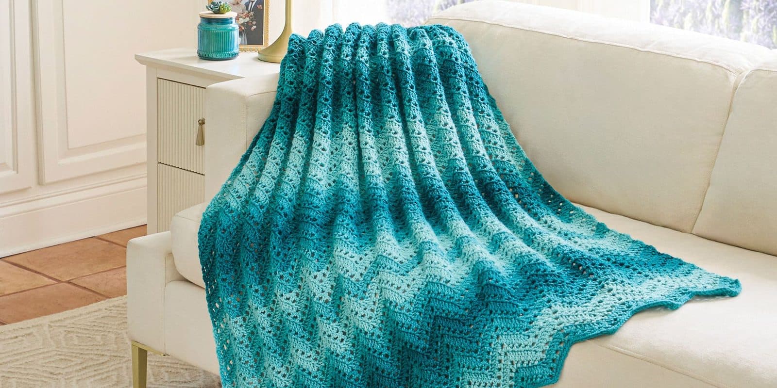 A teal ombre chevron crochet throw draped over a white sofa
