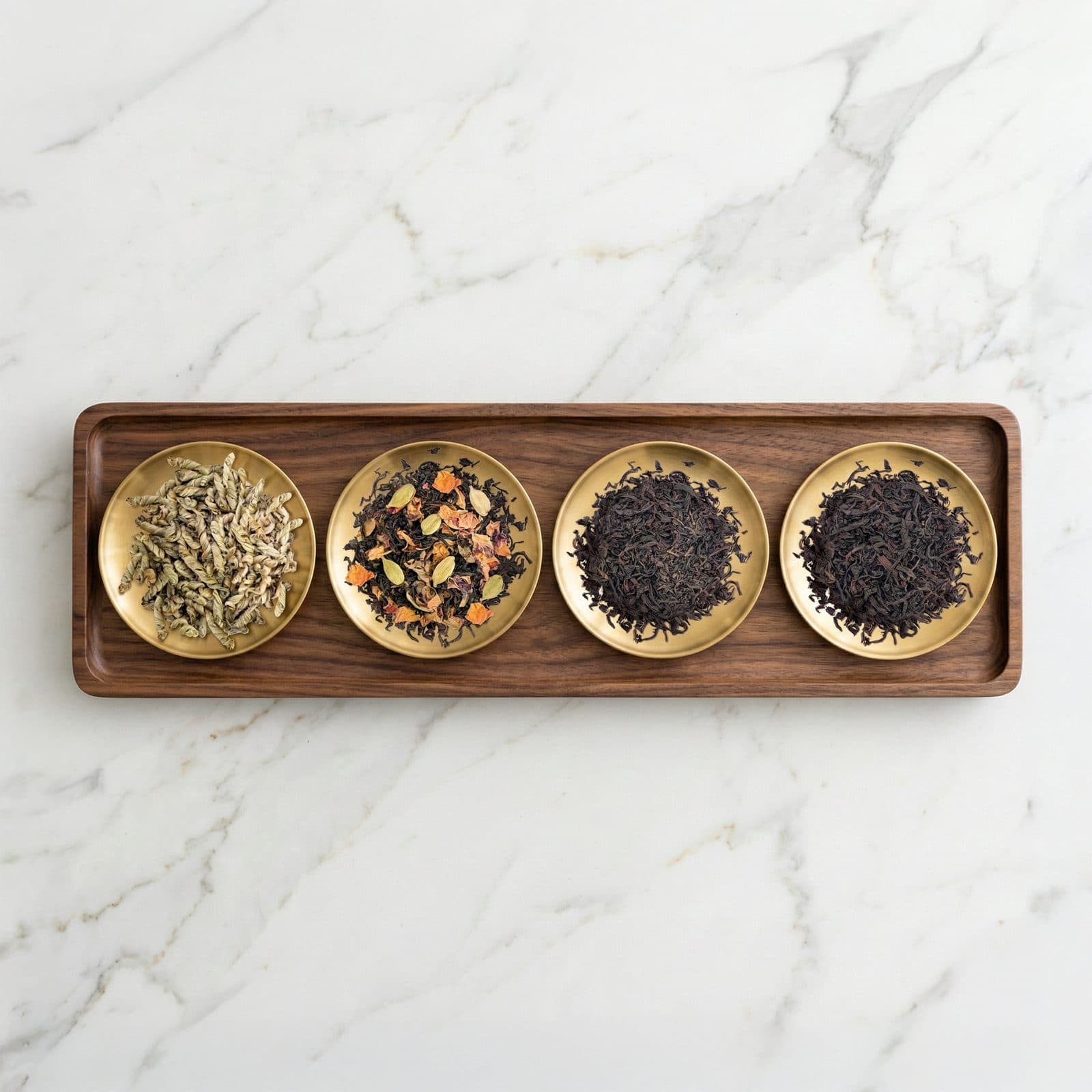 Four loose leaf teas on small brass dishes in a long walnut tray on white marble