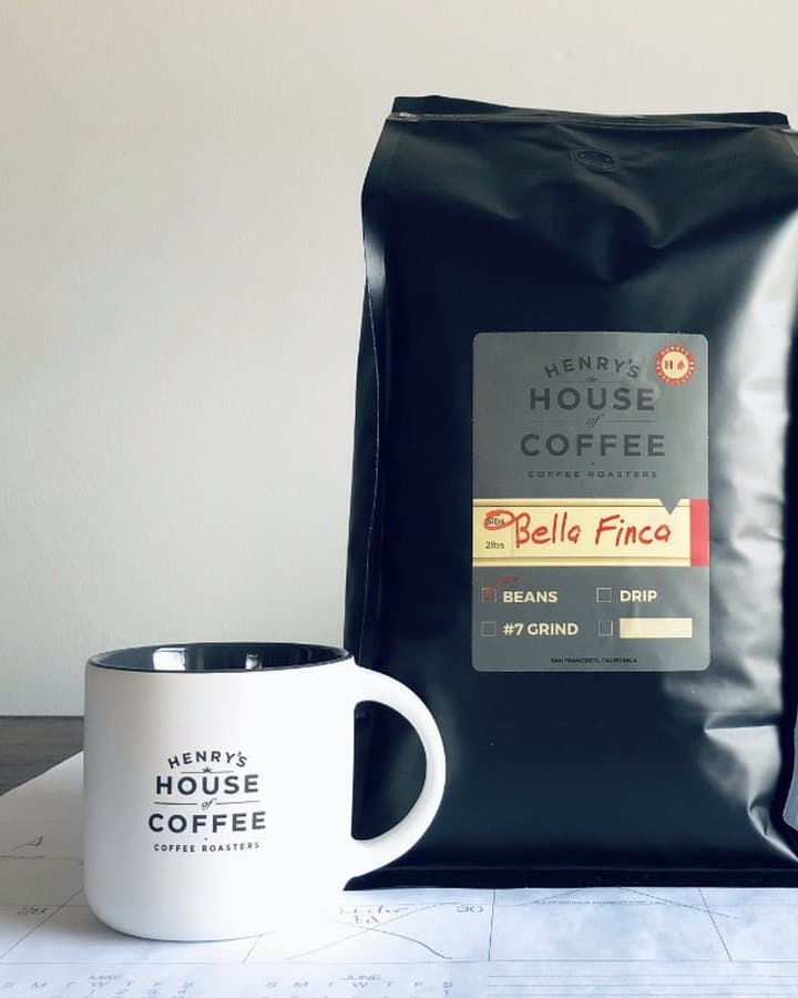 A black Henry's House of Coffee bag of Bella Finca beans beside a white Henry's mug.