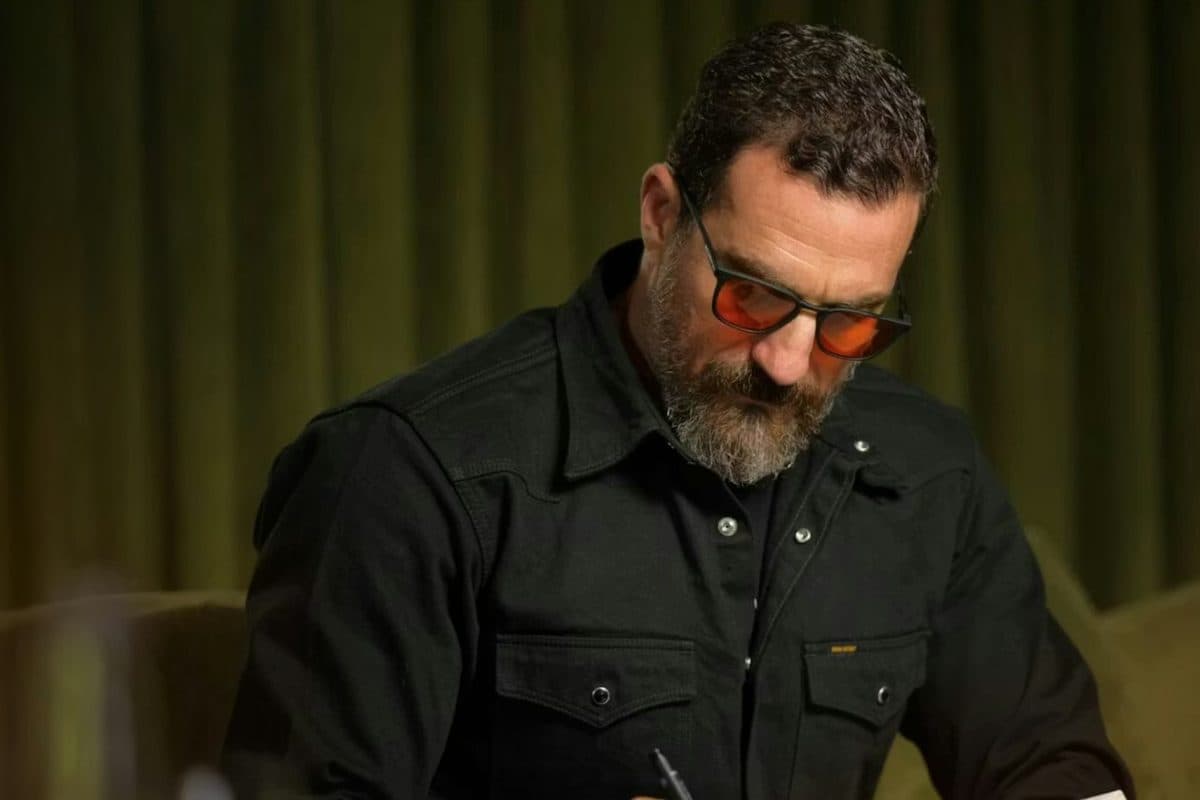 A man in ROKA glasses with red lenses writing at a desk in a dark green room.