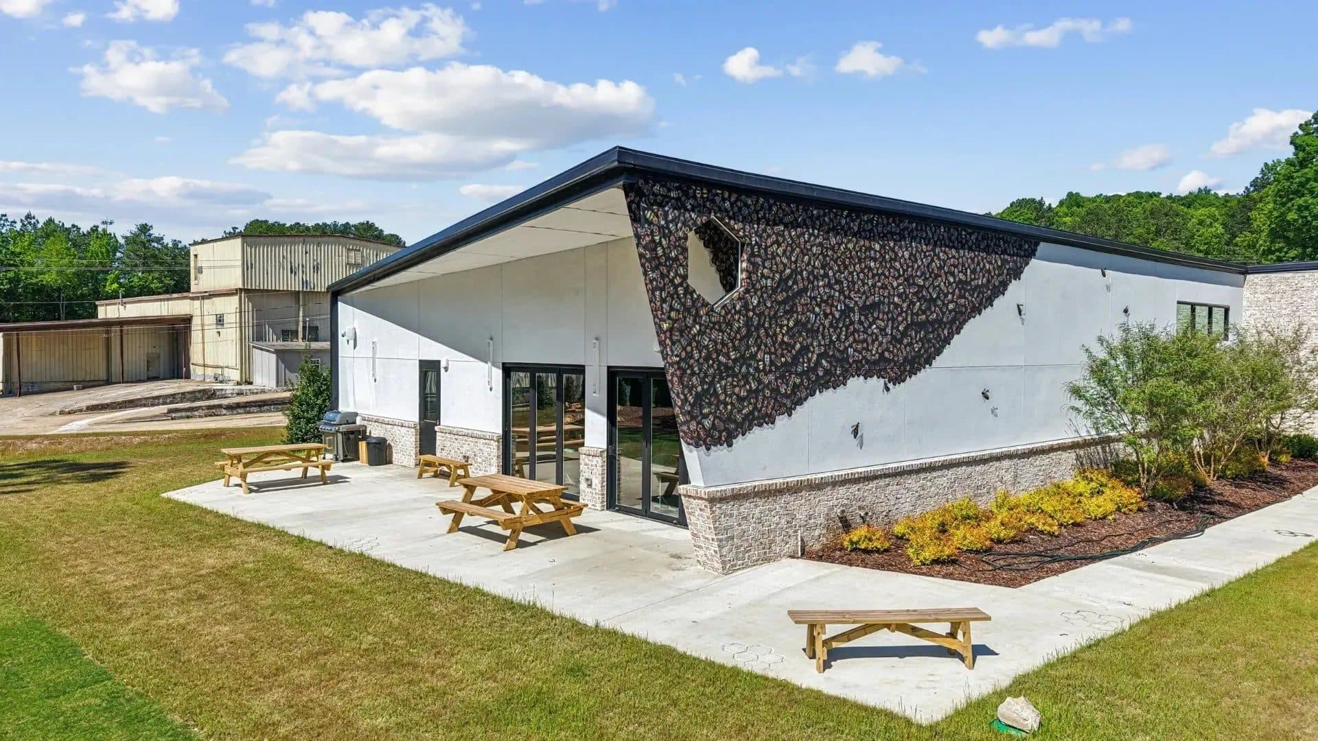 Foxhound Bee Company's white building with a painted swarm of bees spilling down one wall, picnic tables on the patio and a blue sky above.